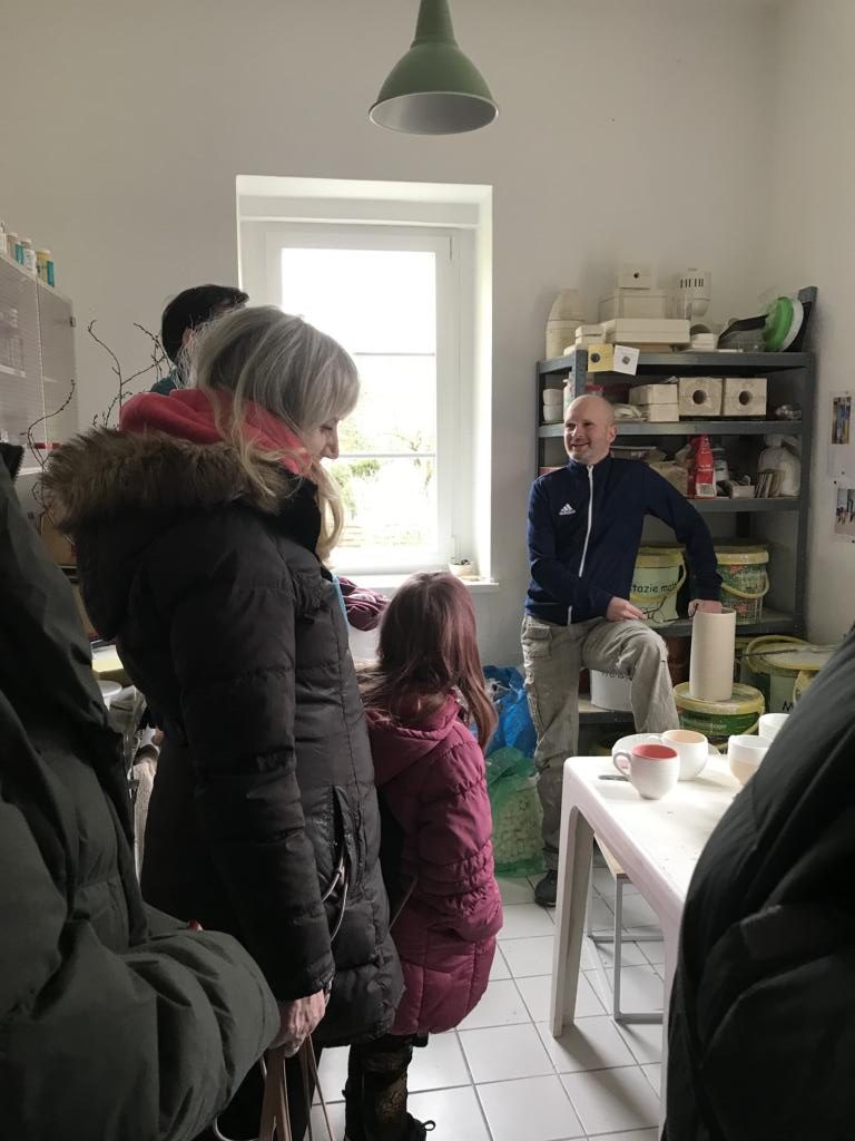 Michael Sommer (im Hintergrund) spricht über seine Werkstatt, die Ausstellung und besondere Ereignisse. Es sind viele Gäste da, die interessiert zuhören. Man trifft sich in der Werkstattküche und durchstreift danach auch die Räume der Ausstellung.