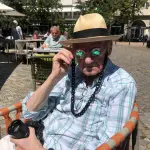 Ralf Krüll ist Starfotograf in der Berliner Szene und weit darüber hinaus. Das Bild zeigt ihn, wie er die Prisma-Brille aufprobiert. Die Sonne scheint auf sein hellblau-weiß-kariertes Hemd.