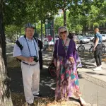 Der Haus- und Hoffotograf Peter Grothe ist regelmäßig beim Walk of Glam dabei. Er steht mit Lilo Rödder unter einem Schatten spendenden Baum.