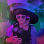 Stella Ahangi verdoppelt sich im Prismaglas. Sie trägt den ausladenden schwarzen Hut aus den 70igern.