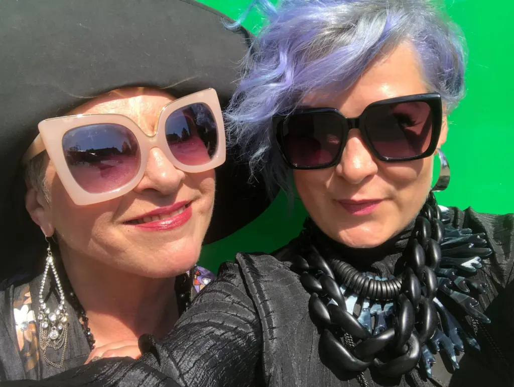 Stella beim hautfarbener großflächiger Designerbrille und Daria mit großer schwarzer Designer-Sonnenbrille und fliederfarbenem Haar