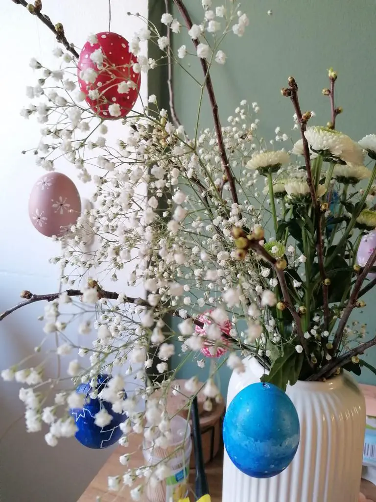 An blühenden Kirschzweigen in der weißen Vase hängen bunte Ostereier. So möchte es die Tradition.