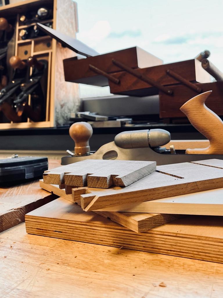 Latten verschiedener Hölzer liegen übereinander, daneben der Hobel und der offene Werkzeugkasten. So beschreibt sich der Werkstattalltag: eine Mischung aus kreativem Gestalten, präziser Handarbeit und manchmal auch viel Geduld.