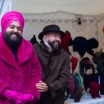 Gianni in pinkem Turban und Pelz neben Carlos – ein Duo, das Mode zur Begegnung macht und Hüte zur Haltung.