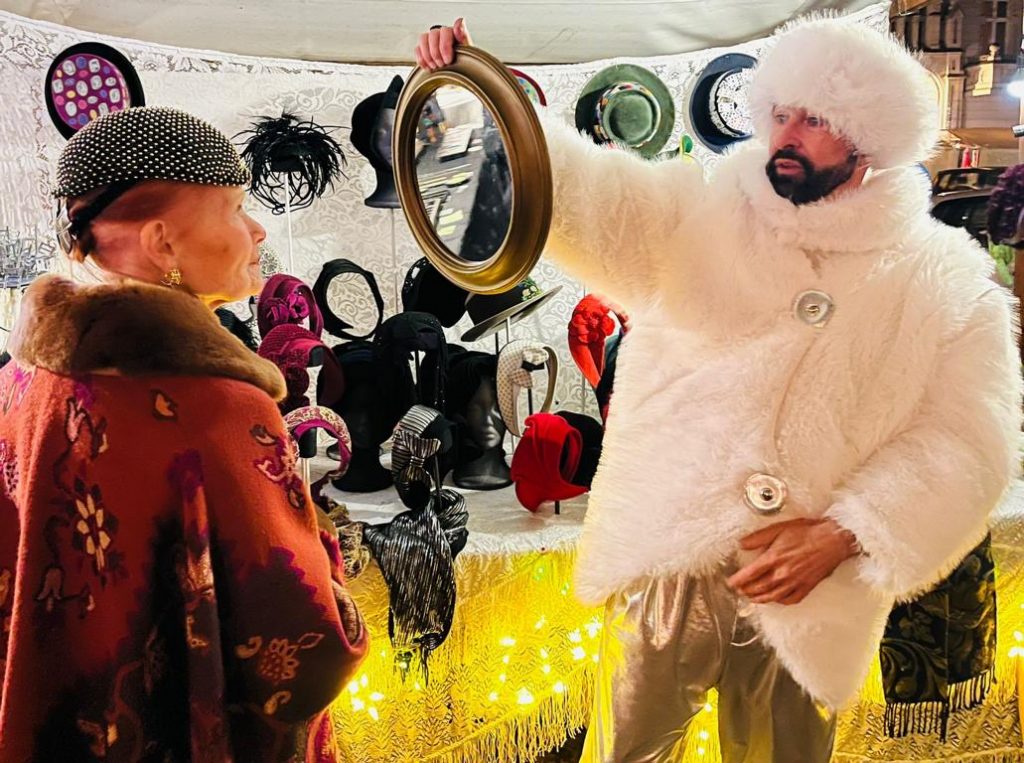 Carlos bei einem der Weihnachtsmärkte von Family & Friends e. V. – im weißen Pelz, als russischer Zar inszeniert, hält der Kundin den Spiegel hin.