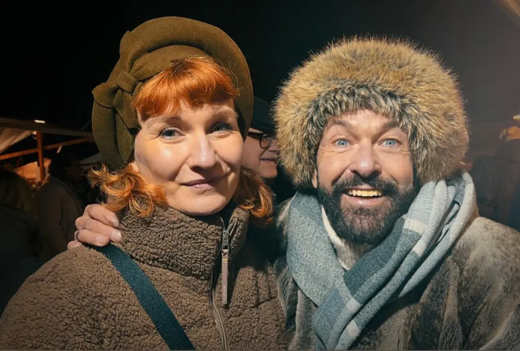 Carlos und eine Kundin beim WEInachtsmarkt 2025 – beide lächeln, die neue Kopfbedeckung sitzt perfekt.