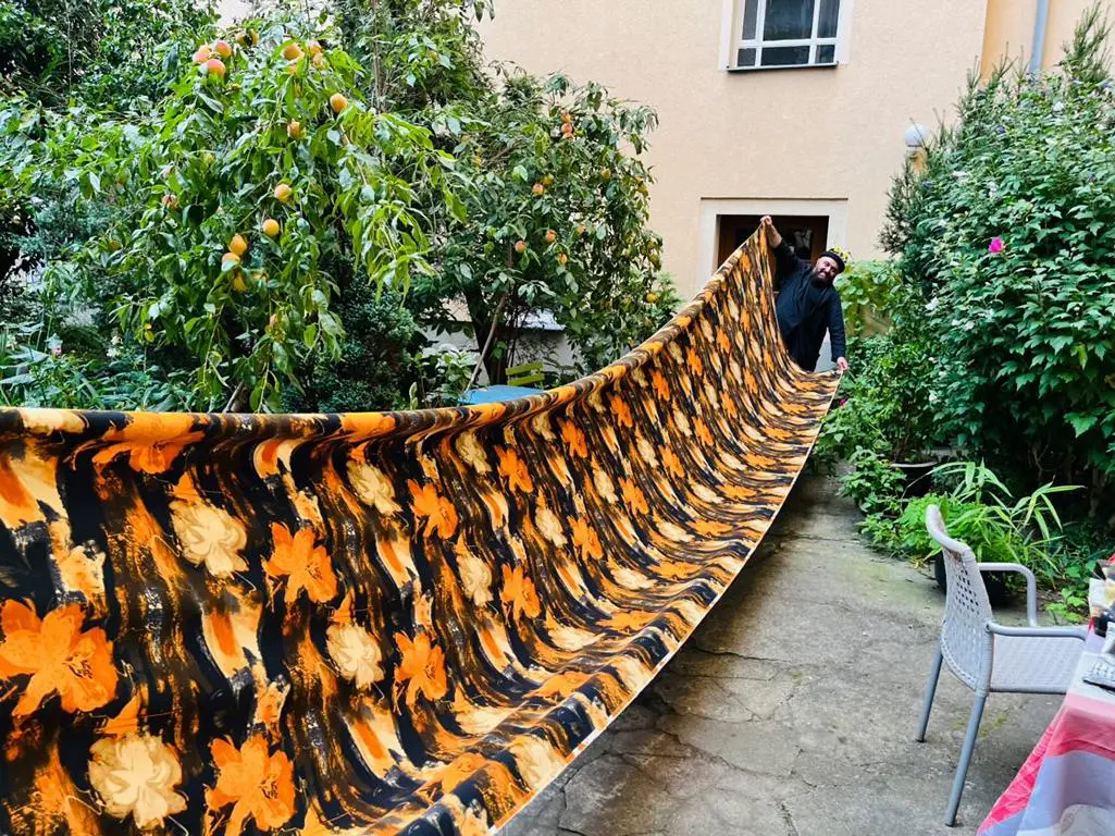Carlos präsentiert ein übergroßes Stoffkunstwerk im Garten – florales Muster trifft auf mediterrane Leichtigkeit im Hofgarten der beiden Künstler Gianni und Carlos Klein.